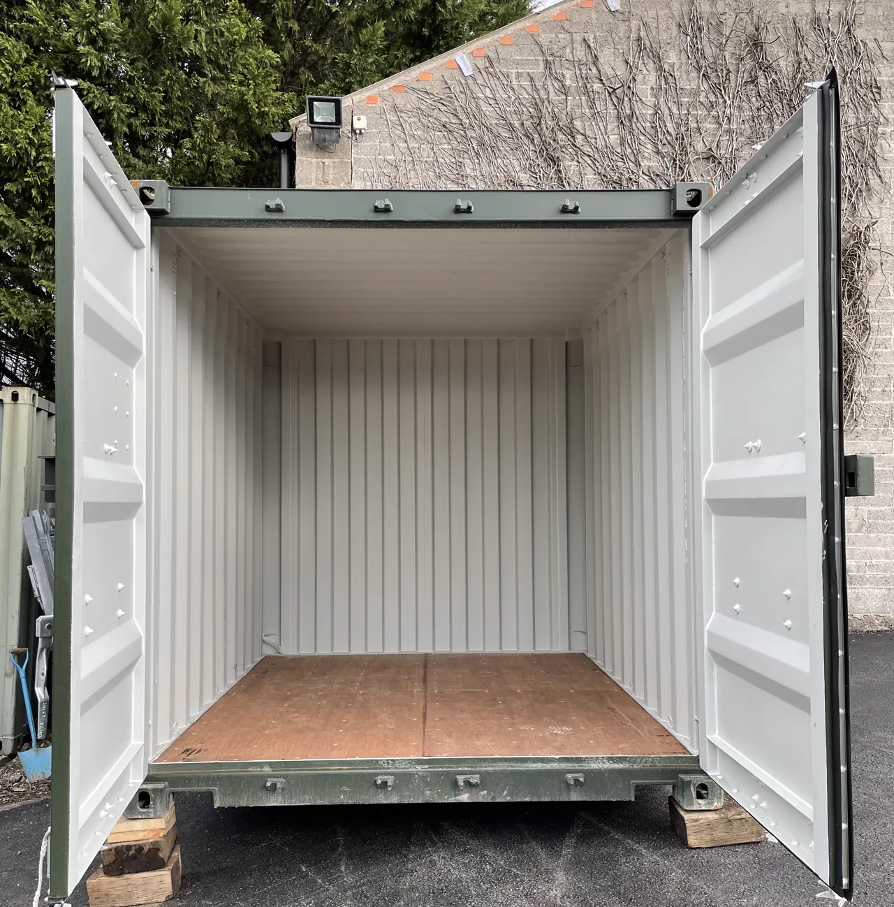 A clean, empty steel storage container with its doors open, painted grey inside with a timber floor